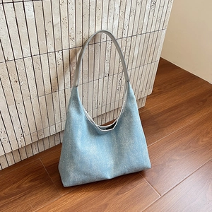 Blue canvas hobo tote bag with silver leather strap against a stone brick wall