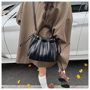 Street view of a black ruched cloud bag worn crossbody with brown blazer