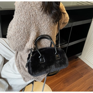 Detail of plush black faux fur handbag with circular leather handle on a beige sweater