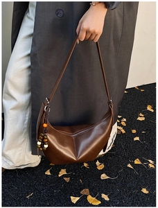 Détail du sac demi-lune en cuir marron avec breloque en bois et feuilles d'automne