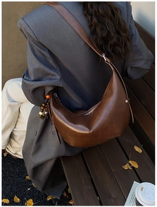 Détail du sac hobo en cuir marron foncé avec breloque perlée sur un banc d'automne