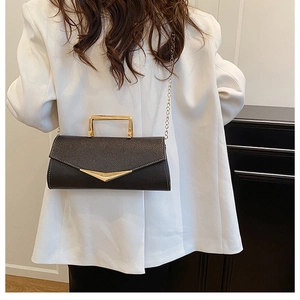 Litchi pattern black leather clutch with gold handle worn on a white blazer