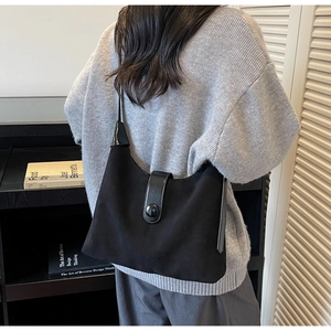 Detail of minimalist black suede shoulder bag with a stylish round buckle on a grey sweater