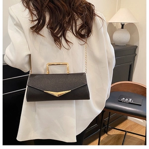 Detail of black pebbled leather crossbody bag with V-shaped gold clasp and chain strap