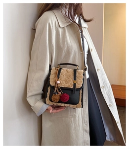 Detail of plush beige and black leather crossbody bag with a plaid pompom charm and metal clasp
