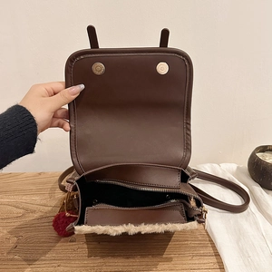 Detail of brown faux leather bag showing magnetic buckle, zipper and plush trim texture