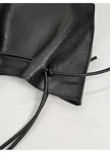 Detail shot of black textured leather crossbody bag with drawstring closure and pleats