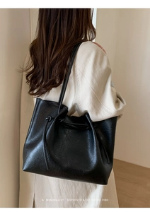 Detail of large black tote bag with drawstring closure worn with a beige trench coat