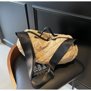 Detail of beige quilted dumpling shoulder bag with black strap on a leather chair