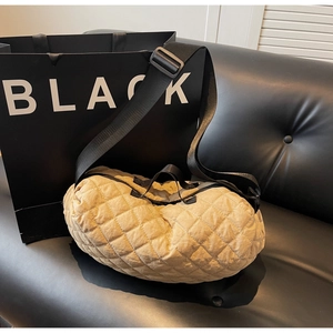 Close-up of quilted khaki dumpling bag with wide black strap on leather sofa