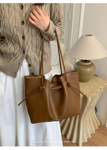 Brown leather tote bag with unique knot detail on shoulder strap in a retro setting