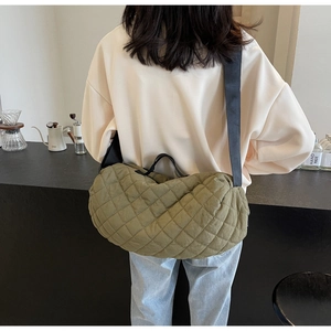 Detailed view of the olive green quilted shoulder bag with wide black strap on a model