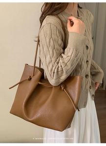 Detail of a brown leather tote bag showing side drawstring knots and textured finish