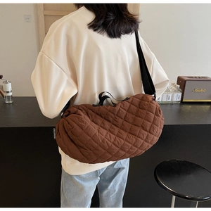 Detail of a large brown quilted crossbody bag with adjustable strap and brand tag