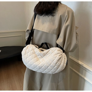 Detail view of white quilted dumpling bag with black strap and side brand label