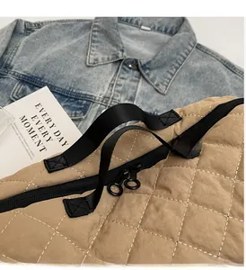 Detail of khaki quilted tote bag with black straps and round zipper pulls on denim backdrop