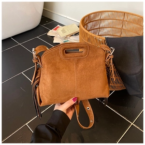 Detail of caramel suede handbag featuring side tassels and oval cutout handle in lifestyle setting