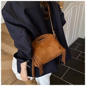 Detail of vintage brown suede crossbody bag with long tassels on a model with blazer