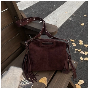 Detail of dark coffee tassel shoulder bag with metallic eyelets on a wooden bench