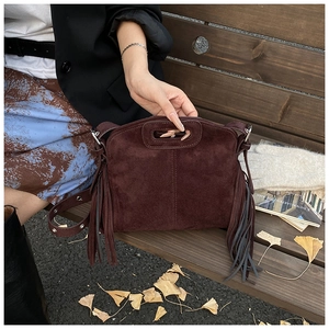 Detail of dark brown suede tassel bag with cut-out handle on a wooden bench