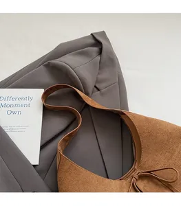 Detail of a brown suede tote bag featuring a decorative bow tie and smooth shoulder strap