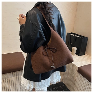 Model wearing a large dark brown suede hobo tote bag with a stylish bow decoration