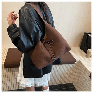 Close-up of brown suede tote bag featuring a bow tie design and silver metal beads
