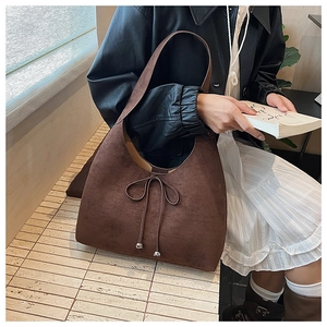 Detail of dark brown suede tote bag with stylish bow tie and silver metal ball accents