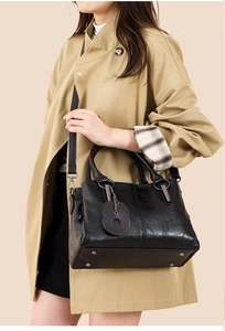 Detail of black leather tote bag featuring metal feet and round leather charms