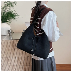 Detail of a large black suede tote bag with decorative bow and drawstring feature