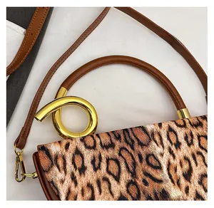 Detail of leopard print handbag featuring a gold ring handle and removable brown strap