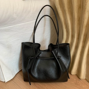 Minimalist large black tote bag with drawstring detail and matte leather texture on floor