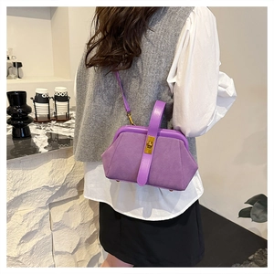 Detail of purple matte shell handbag with gold twist lock worn by model on shoulder