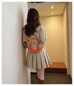 Close-up of orange leather crossbody bag with leopard print flap and gold ring hardware