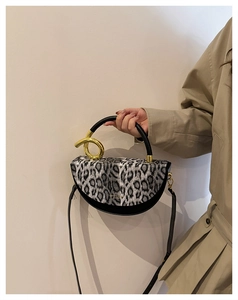 Detail of leopard print handbag with artistic gold twisted metal handle and saddle design