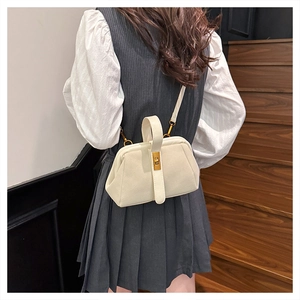 Detail of a creamy white shell bag with a gold twist lock and a crossbody strap