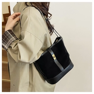 Detail of black bucket bag with gold clasp closure and mixed leather texture on model