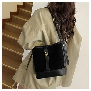 Detail of a black leather bucket bag with gold buckle shown on a model's shoulder