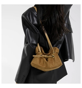 Brown suede crossbody bag with drawstring closure and gold eyelets shown on a model