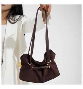 Detailed view of dark brown suede handbag featuring gold rings and drawstring accents