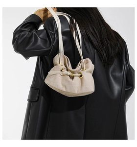 Detail of beige suede drawstring shoulder bag with gold eyelets on a black leather jacket