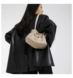 Detailed view of beige suede shoulder bag with cream straps on a model in black leather jacket