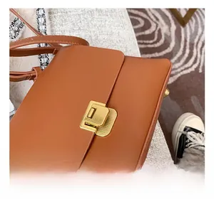 Gros plan sur la boucle en métal doré et le cuir texturé d'un sac bandoulière marron