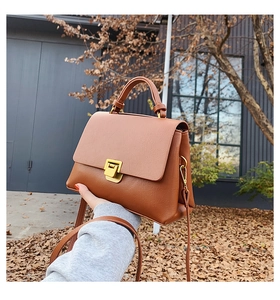 Detail of brown PU leather crossbody bag with gold buckle in an autumn street setting