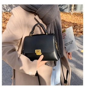 Close-up of black leather handbag with gold metal lock and detachable shoulder strap