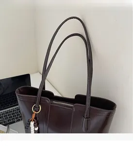 Close-up of brown leather tote bag with sturdy shoulder strap and wooden bead charm