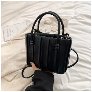 Detail of vertical pleated black leather handbag with golden hardware and twin handles