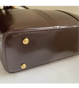 Detailed close-up of dark brown leather handbag base with gold protective metal feet