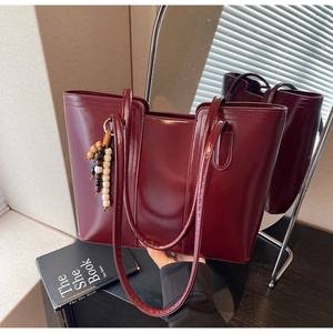 Detail of burgundy glossy tote bag featuring contrast stitching and wooden bead charm