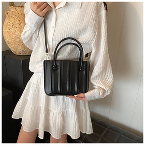 Detail of black pleated crossbody bag with gold hardware shown on a model in white shirt
